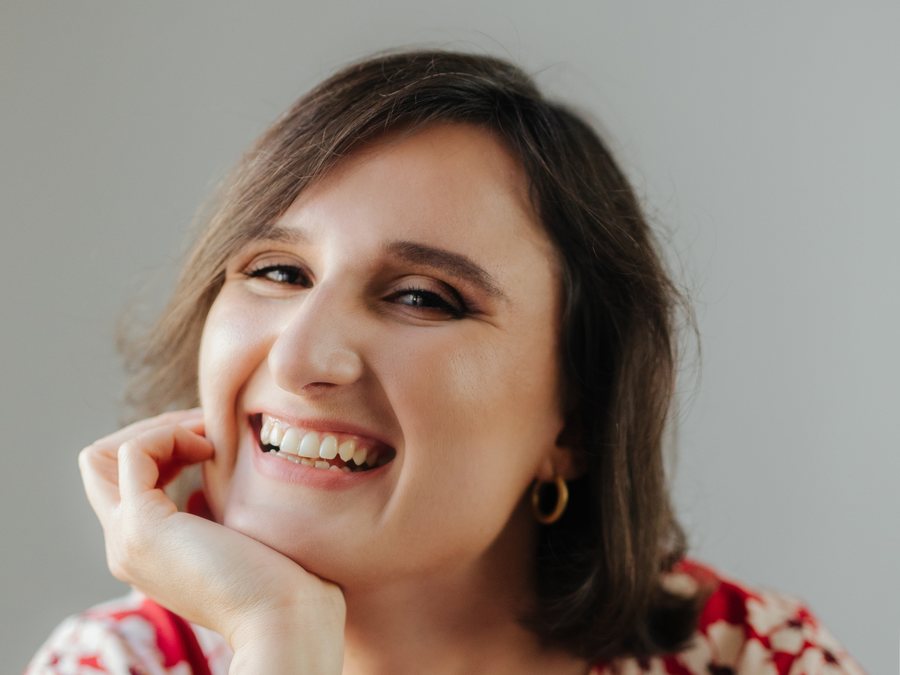 Szeroko uśmiechnięta nauczycielka włoskiego online, Kasia Brol, właścicielka szkoły Meriggiare, pozująca w studiu w letniej, czerwonej sukience w kwiaty